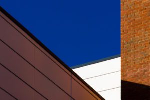 Red brick, brown and white cladding with blue sky by Steve Parker